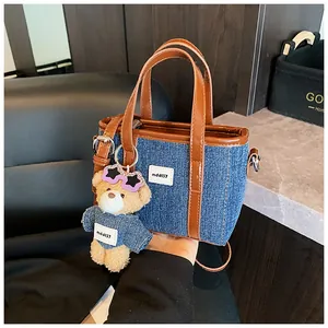 Detail van een denim emmer tas met lederen bekleding en schattige pluchen beer hanger.