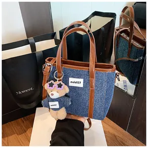 Detailweergave van denim emmer tas met bruine lederen rand en schattige beer tas hanger