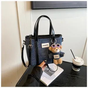 Detailopname van een blauwe denim emmerhandtas met een schattige teddybeerbedel