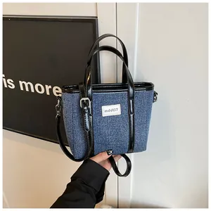 Gedetailleerde opname van een blauwe denim emmer tas met stijlvolle zwarte glanzende bies