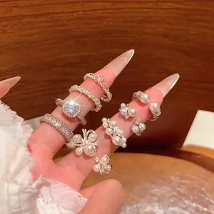 Detailed view of various French lace rings with pearls on manicured fingers.