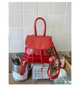 Fashionable red mini leather backpack with cherry charm displayed in a modern cafe setting
