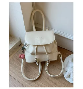 Chic cream mini backpack featuring a drawstring flap and a decorative red cherry charm