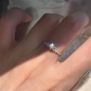 Close-up of a delicate French lace style silver ring with a sparkling center stone on a finger.