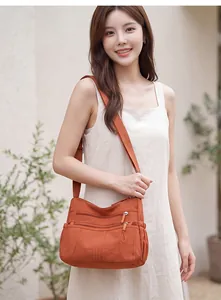 Orange multi-pocket crossbody bag for women displayed by a model in a garden