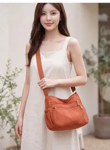 Detailed view of a large multi-pocket orange nylon crossbody bag worn by a model