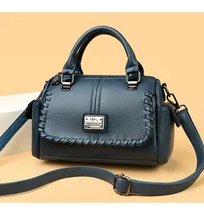 Detail view of deep teal leather handbag with braided edges and metal logo icon