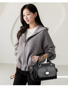Detailed view of a professional black leather handbag held by a woman in a grey hoodie