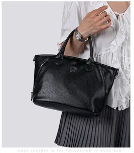 Detailed view of a vintage black pebbled leather handbag held by a model in white blouse