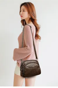 Detail view of a brown pebbled leather shoulder bag worn by a model in a pink sweater