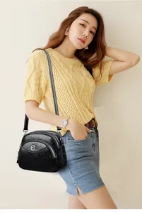 Close-up detail of a classic black three-layer leather crossbody bag on female model