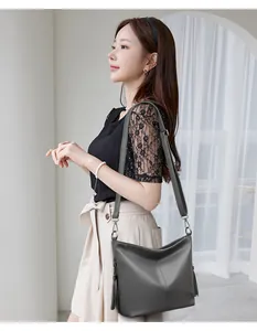 Side view of a dark grey pebbled leather crossbody bag with decorative side tassels.