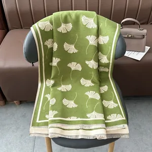 Dettaglio ravvicinato di sciarpa verde con motivo a foglie di ginkgo e frange morbide