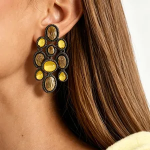 Close-up detail of retro ethnic statement earrings with yellow resin worn on model's ear.