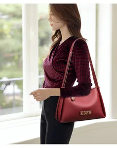 Close-up of elegant red leather shoulder bag worn by model in a stylish indoor setting.