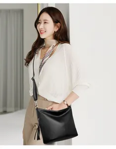 Elegant Asian model showcasing a black textured leather crossbody bag with tassel detail