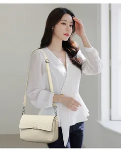 Stylish cream crocodile texture crossbody bag modeled with a white blouse and trousers.