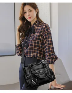 Sac cabas en cuir noir avec rivets et poignées, porté par un mannequin en chemise à carreaux.