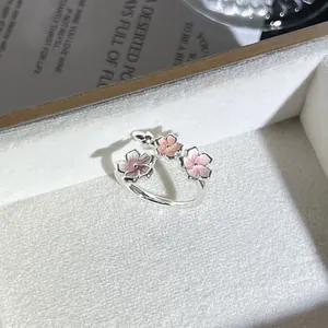 Primer plano detallado de un elegante anillo abierto plateado con tres flores rosas en 3D
