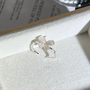 Vista detallada de un anillo abierto plateado con flor de mariposa rosa y borde perlado.