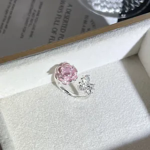 Primer plano de anillo abierto de plata con flor rosa y mariposa de cristal.