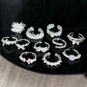 Group of silver-finish rings featuring pearls and bow designs on reflective surface