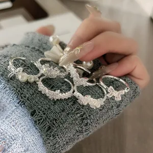 Nahaufnahme eleganter Silberringe mit Perlen und Schleifen auf einem Strickärmel