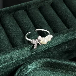 Detailed view of an elegant silver bow ring with pearls on a green velvet jewelry stand