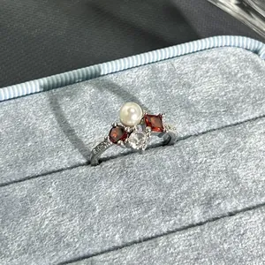 Detail shot of a silver ring with red gemstones and a pearl in a blue velvet box