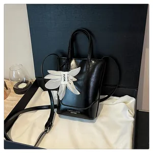 Elegant black leather bucket bag with white flower charm displayed in a luxury gift box
