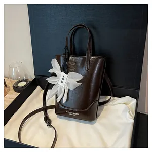 Glossy dark brown bucket bag with a white floral charm, presented in a black gift box.