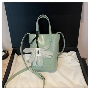 Close-up of a stylish light green bucket bag featuring a white petal charm in a black gift box