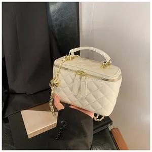 Detalle de bolso acolchado crema con cadena dorada y colgante de bola metálica