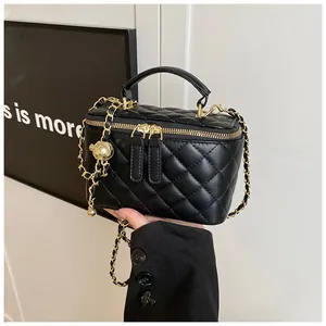 Detalle de un mini bolso acolchado negro con correa de cadena dorada y colgante de bola