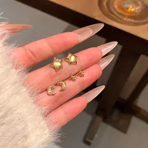 Close-up detail of dainty gold star and moon stud earrings with pearl accents on fingers