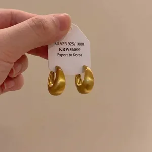 Close-up detail of brushed golden hoop earrings featuring a 925 silver hallmark card