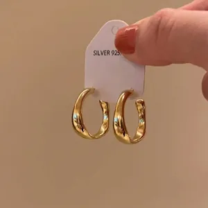 Close-up of chunky gold hoop earrings featuring a shiny finish and S925 silver mark on the tag