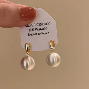 Close-up of elegant gold-toned drop earrings featuring brushed white spherical beads