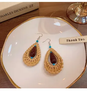 Detail view of ethnic rattan teardrop earrings with turquoise beads on a ceramic plate