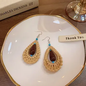 Bohemian handmade rattan woven water drop earrings with turquoise beads on ceramic plate.