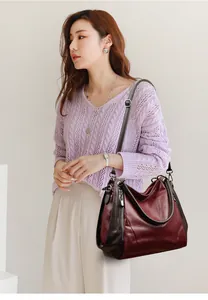 Elegant Asian model carrying a large burgundy soft leather shoulder bag in a studio.