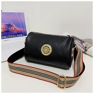 Dettaglio borsa a barile in pelle nera con emblema dorato e tracolla a righe colorate.