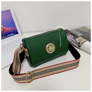 Dettaglio di una borsa a cilindro in pelle verde con emblema dorato e tracolla a righe