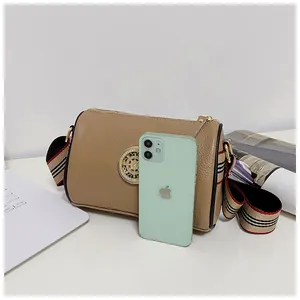 Borsa a tracolla cilindrica in pelle kaki accanto a uno smartphone per le misure.