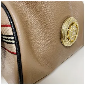 Dettaglio di una borsa in pelle martellata con hardware dorato e tracolla a righe.