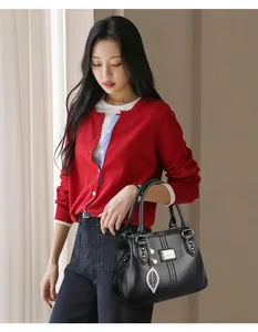 Detail view of a black pebbled leather handbag with a leaf charm held by an Asian model