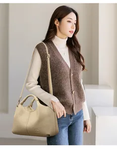 Detailed view of a premium beige pebbled leather handbag with twin handles on a model