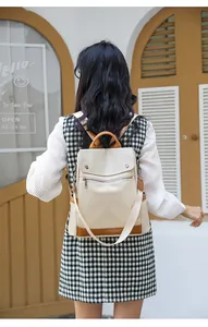 Back view of a stylish cream canvas backpack with brown trim for women in a cafe
