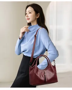 Detail view of a burgundy soft leather handbag held by a model in a light blue top