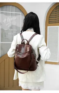Rear view of a stylish brown leather anti-theft backpack worn by a woman outdoors.